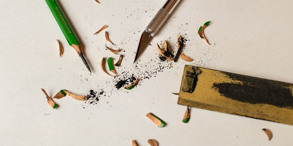Graphite pencil, X-Acto knife and sandpaper block surrounded by pencil shavings